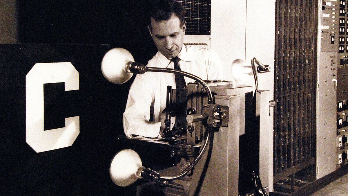 A man adjusts the Mark I Perceptron, a 1960 experimental machine that learned to recognise letters, beside a large white letter C.